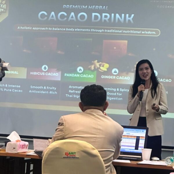 ผู้ประกอบการหญิงนำเสนอแผนธุรกิจผลิตภัณฑ์ Premium Herbal Cacao Drink บนเวที R2G Northern Pitching ณ E-Library มหาวิทยาลัยราชภัฏพิบูลสงคราม จ.พิษณุโลก โดยมีคณะกรรมการนั่งฟังด้านหน้า หน้าจอแสดงรายละเอียดรสชาติสมุนไพรเช่น Ginger Cacao และ Pandan Cacao