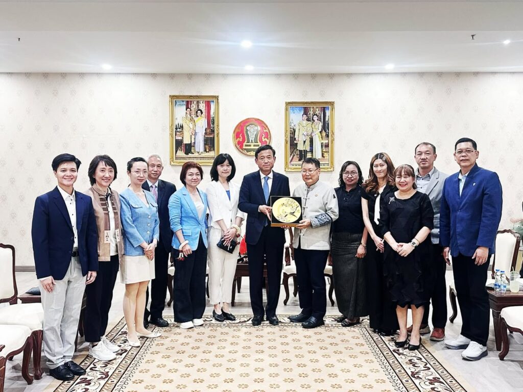 ภาพหมู่คณะผู้แทนไทยและจีน โดยตัวแทนหลักตรงกลางร่วมกันถือของที่ระลึก จานเซรามิกมงคลสีทองฉลุลาย ด้านหลังประดับพระบรมฉายาลักษณ์และตราสัญลักษณ์พระราชวงศ์ไทย
