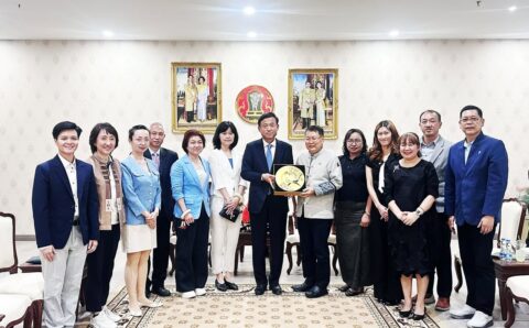 ภาพหมู่คณะผู้แทนไทยและจีน โดยตัวแทนหลักตรงกลางร่วมกันถือของที่ระลึก จานเซรามิกมงคลสีทองฉลุลาย ด้านหลังประดับพระบรมฉายาลักษณ์และตราสัญลักษณ์พระราชวงศ์ไทย