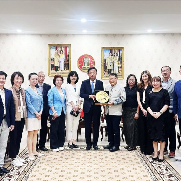 ภาพหมู่คณะผู้แทนไทยและจีน โดยตัวแทนหลักตรงกลางร่วมกันถือของที่ระลึก จานเซรามิกมงคลสีทองฉลุลาย ด้านหลังประดับพระบรมฉายาลักษณ์และตราสัญลักษณ์พระราชวงศ์ไทย