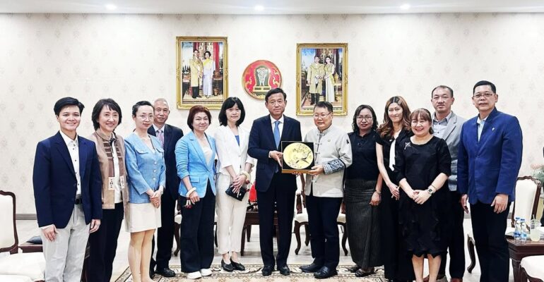ภาพหมู่คณะผู้แทนไทยและจีน โดยตัวแทนหลักตรงกลางร่วมกันถือของที่ระลึก จานเซรามิกมงคลสีทองฉลุลาย ด้านหลังประดับพระบรมฉายาลักษณ์และตราสัญลักษณ์พระราชวงศ์ไทย